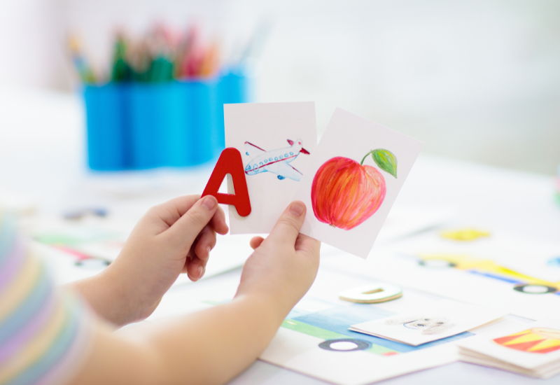 child holding flashcards apple airplane a